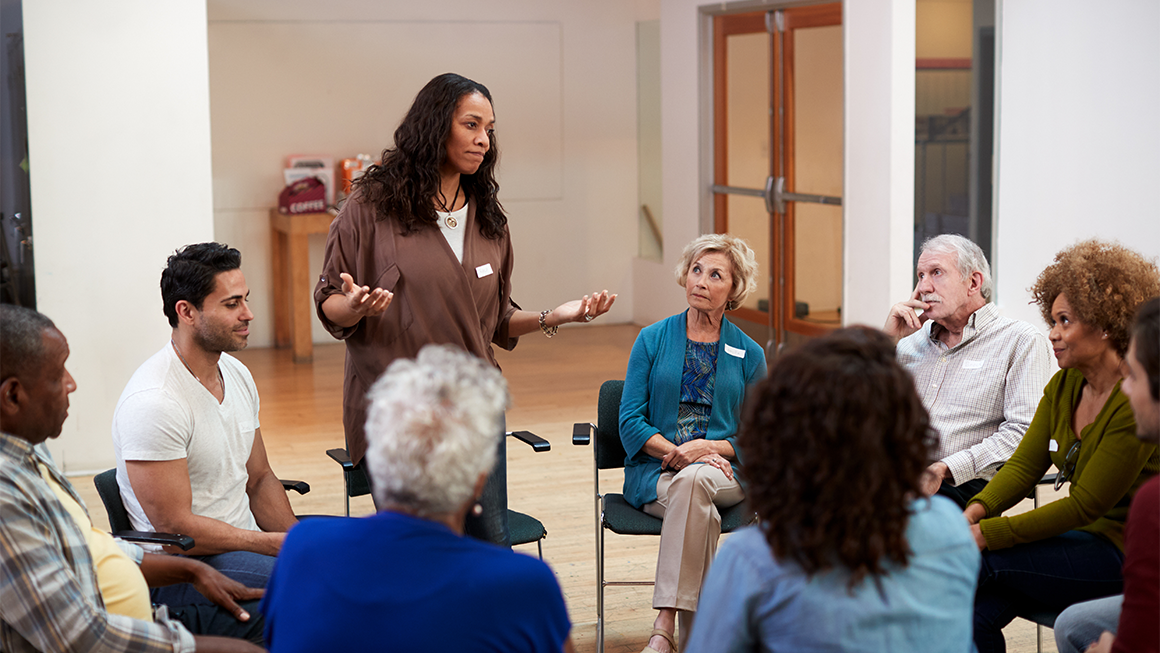 A woman stands to speak at a group therapy session.