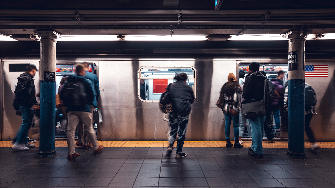 People hurry on and off a subway train at an underground station, with motion blur showing movement as doors stand open and passengers board and exit.