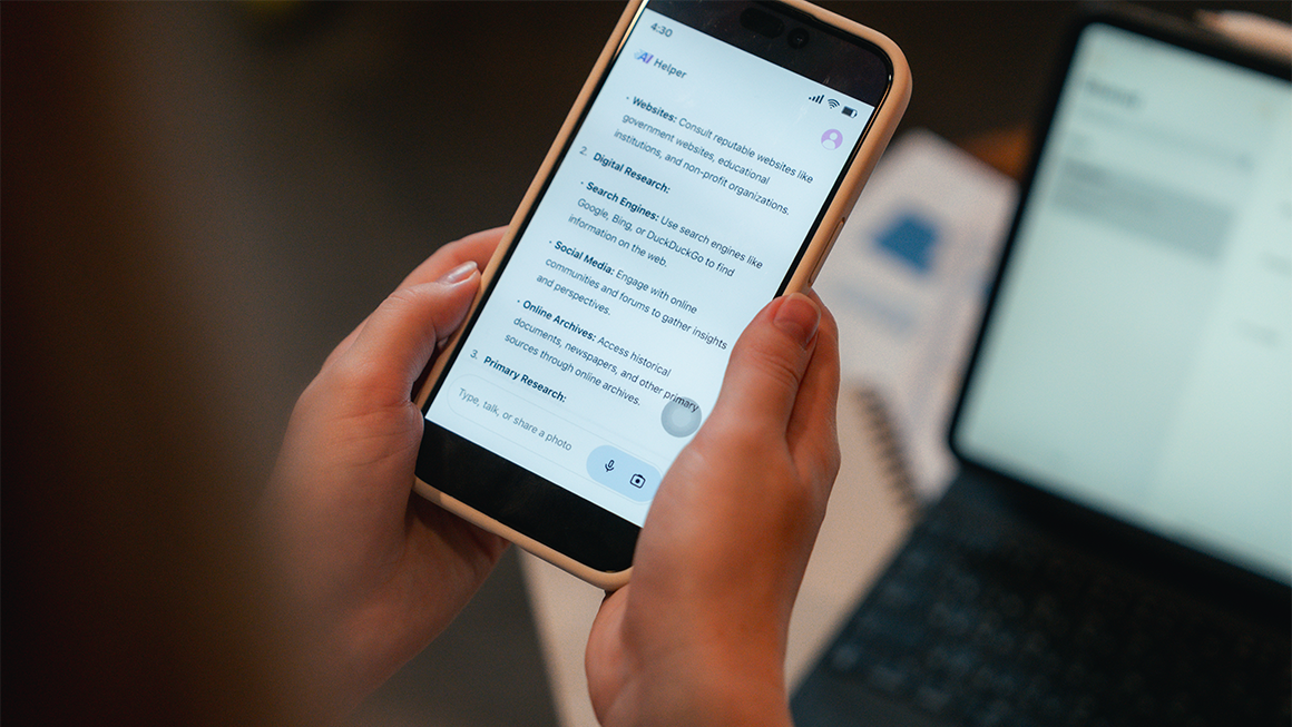 A person holds a smartphone displaying an “AI Helper” chat screen