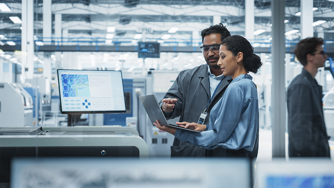 photo of Male Industrial Engineer And Female Supervisor Using Laptop And Talking At An Electronics Factory