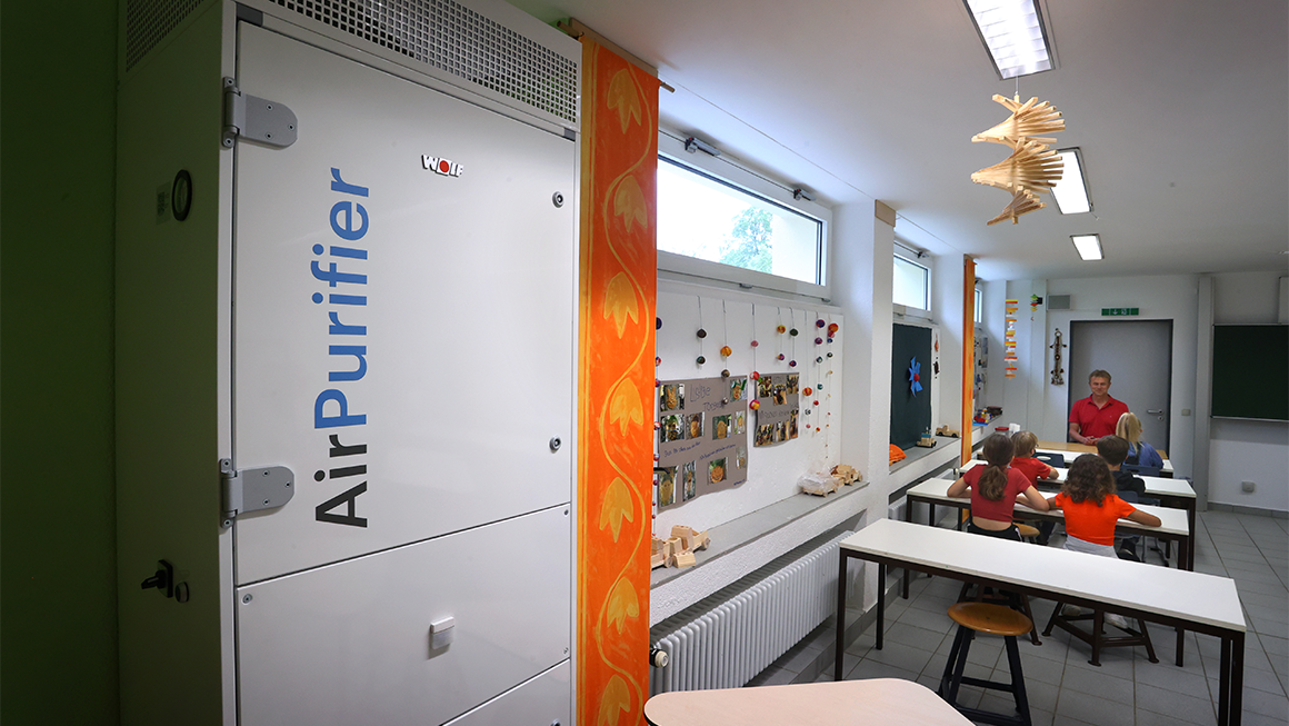 Classroom with students at tables and a large air purification unit installed along one wall.
