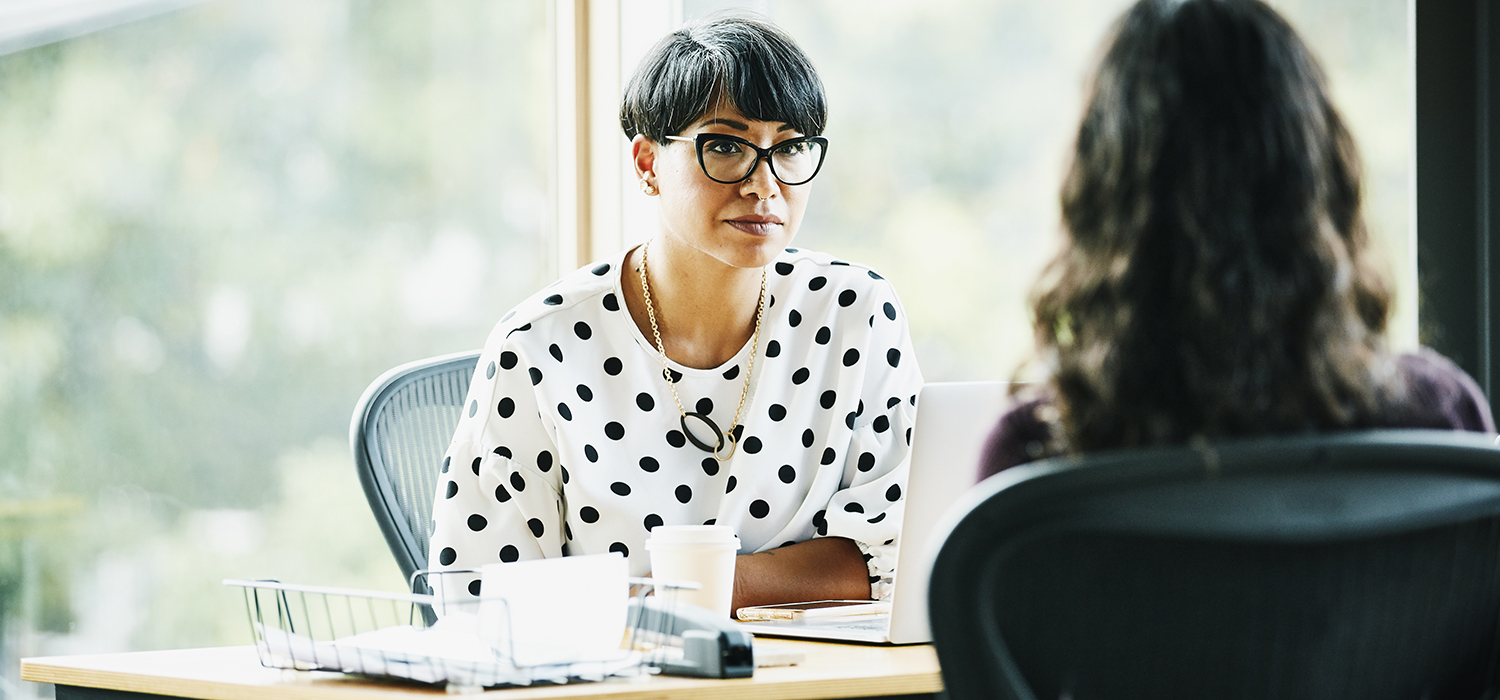 Two people talk at a desk