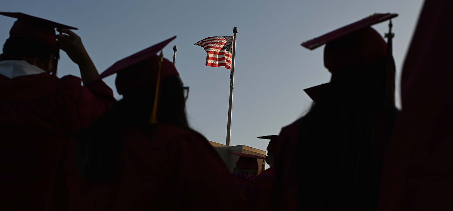 Students graduating from college stand in front of an American flag