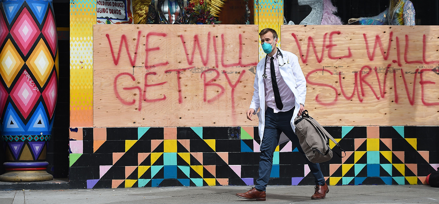 Masked doctor walks past a boarded building