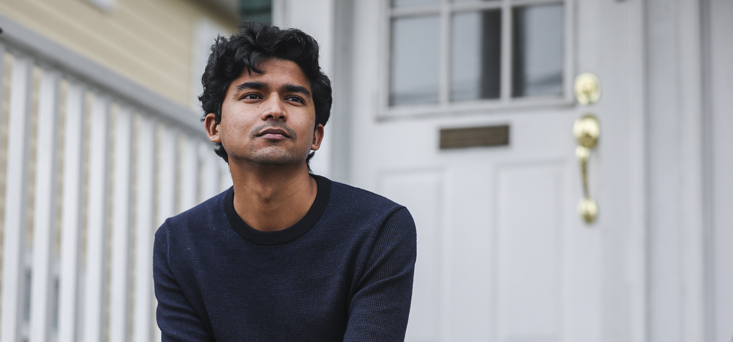Young man poses in front of his home