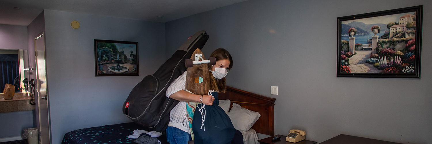 Person experiencing homelessness packs their bags in a hotel