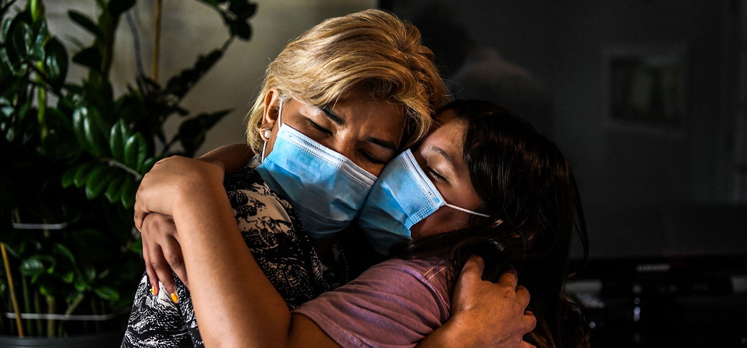 Two women hug while wearing masks