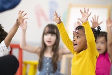 group of preschool students is sitting with their legs crossed on the floor in their classroom