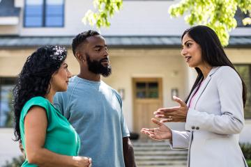 Couple meeting with real estate agent in front of home