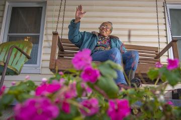 African American woman waving while sitting on front porch 