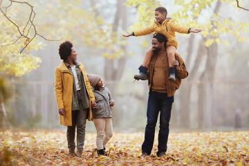 Happy black parents and their kids having fun while spending an autumn day at the park. Father is carrying son on shoulders.