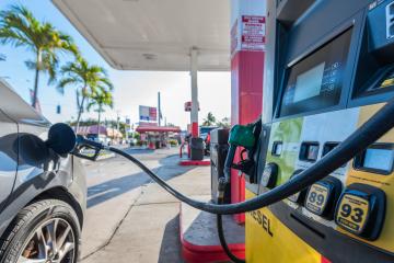 A close-up shot of a gray car at a gas pump, with the nozzle inserted into the filler neck.