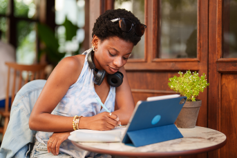photo of a young woman immersed in her digital tablet while enjoying a cup of coffee at a cozy sidewalk cafe