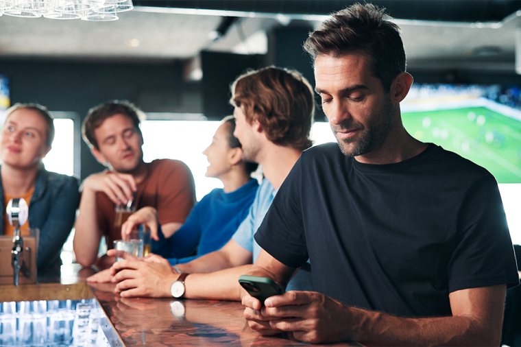 man browsing on smartphone in a pub and sports betting for entertainment