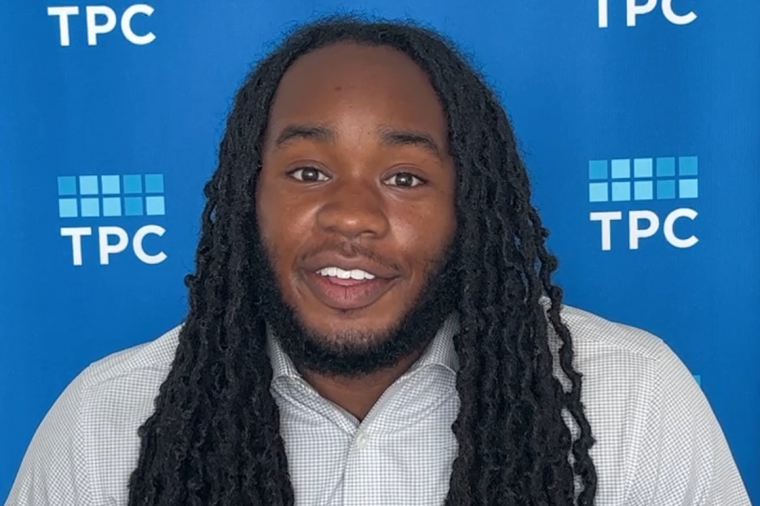 A screenshot of a person looking at the camera in front of a backrop that says TPC