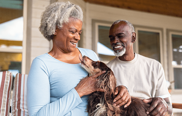 An older Black man and woman sit on a porch holding their dog