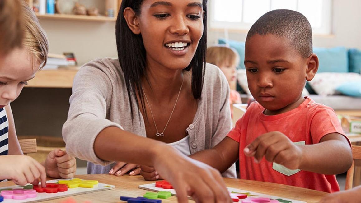 female teacher working at classroom table with four prekindergarten students