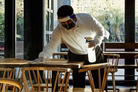 Masked restaurant employee cleans tables