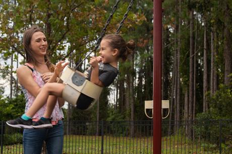 Mother pushing daughter on swings set. 