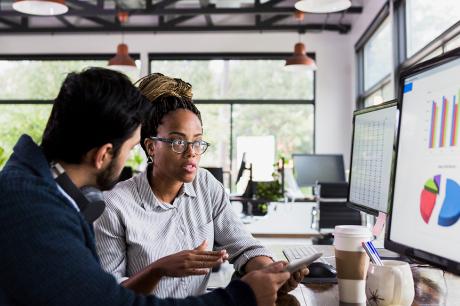 Two people working and looking at graphs on a computer. 