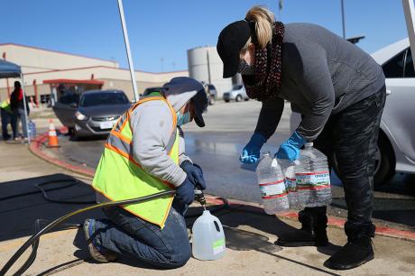 Volunteers fill water jugs for people at a drive-through water distribution center