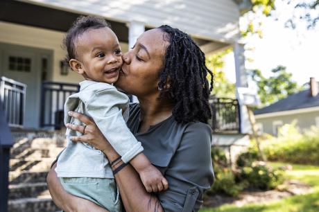 Mother holding child in front of home. 