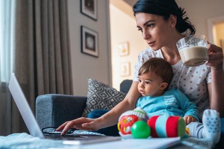 Mother working off a laptop with her child on her lap.
