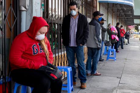 Francisco Montero (center) of Richmond wears a mask while waiting with others in a long line outside of Terra Nova Clinic in the Fruitvale neighborhood of Oakland