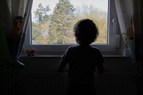 Child in their bedroom looking out their window.