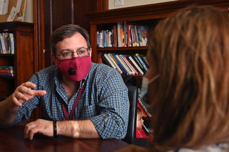 Man in a face mask talking to a women at a table.