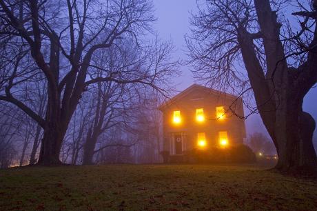 A house with light in the windows sits on the hill in the dark