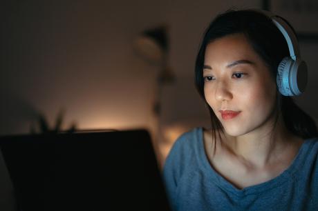 A woman looking at a laptop screen with headphones on. 
