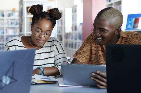 A student and a teacher working together with laptops nearby.