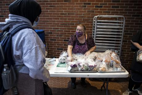 Woman in  a face mask hands out food at school to students.