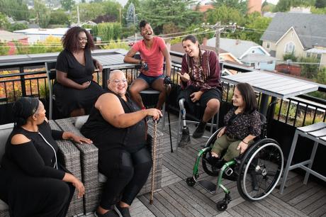 Overhead shot of six disabled people of color at a rooftop deck party.