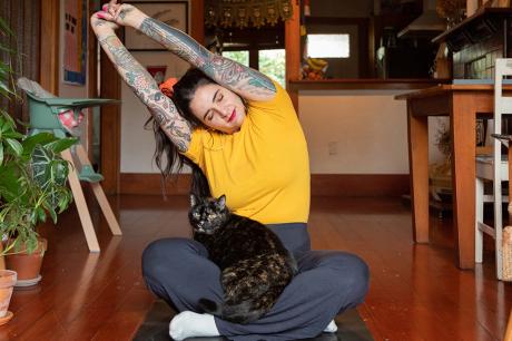 An image of a woman stretching with a cat on her lap. 