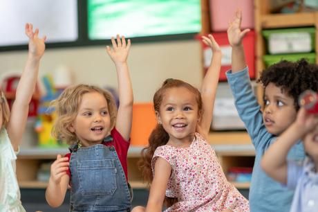 A group of elementary students raising their hands in a classroom