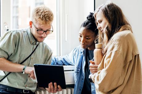 Three young adults huddled around looking at an iPad. 