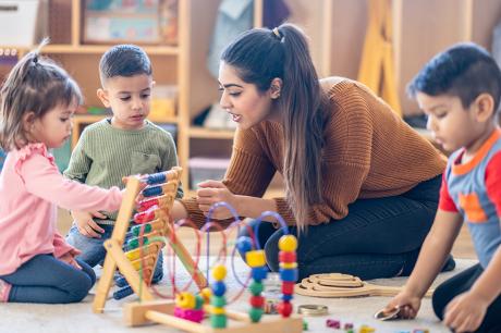 A teacher with a group of children playing on the floor. 