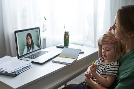 A woman holding her child and talking to her doctor through a laptop.