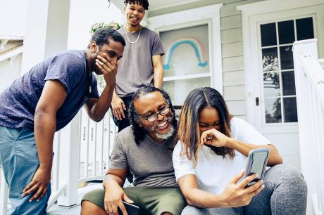 A family on their front steps looking at their mobile phone. 