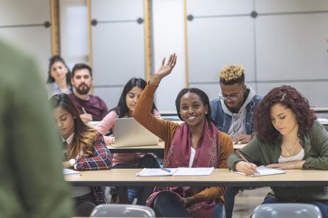 An image of college aged students in a classroom facing the profesor.