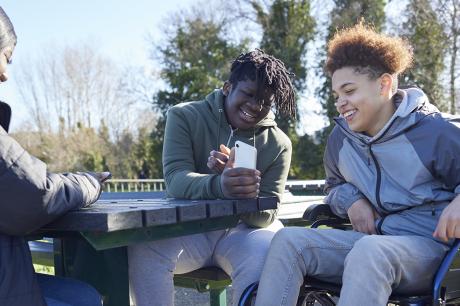 Young boys looking at their phones outside laughing together.