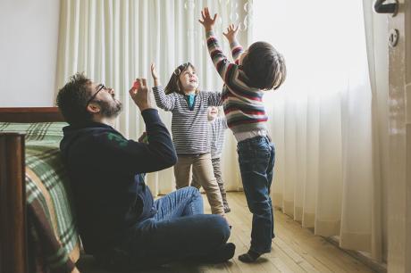 A father playing with his children in the bedroom.