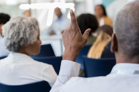 A shot of people sitting in chairs raising their hands.