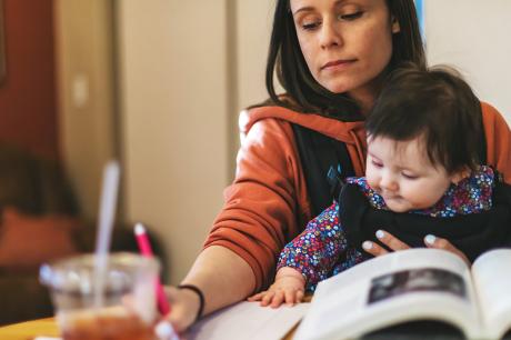 A mother and her child strapped to her front sitting at a table.