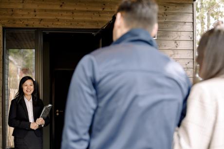 Two people at the front door of an open house and a realtor greeting them.