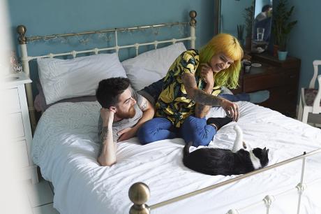Two young adults on a bed playing with a cat.