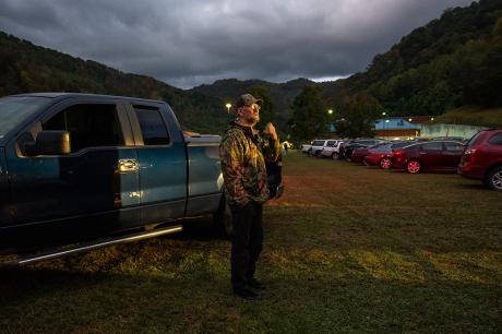 A man outside in a field next to a parked truck.