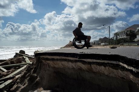 A man in a wheelchair near a beach.